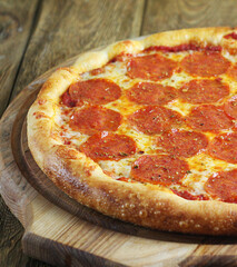 A whole pepperoni pizza lies on a wooden board on a wooden table.