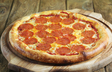 A whole pepperoni pizza lies on a wooden board on a wooden table.