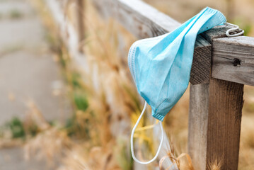 Waste during COVID-19. A blue medical face mask hangs on a wooden fence and is thrown into the...