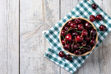 Fresh cherries with water drops in wooden bowl on white wooden table. Top view. Copy space