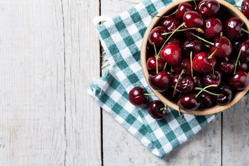 Fresh cherries with water drops in wooden bowl on white wooden table. Top view. Copy space
