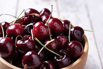 Fresh cherries with water drops in wooden bowl on white wooden table. Close up	