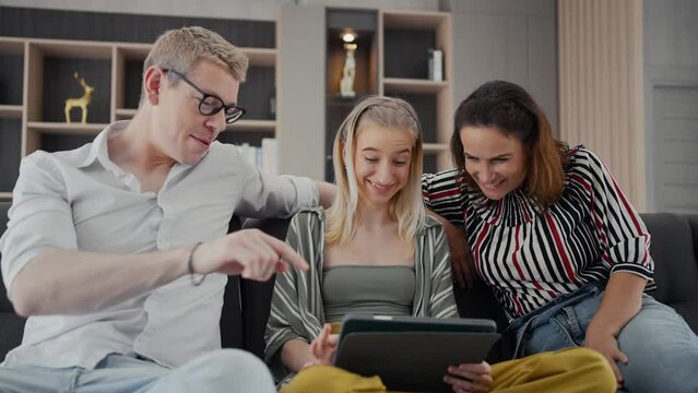 Parents with teenage daughter watching funny videos using laptop browsing online tv streaming enjoying spending time together on weekend at home in living room sitting on sofa.