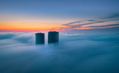 Skyscraper rooftop over the clouds at sunrise. Thick fog covers the Riga city, and warm sunlight...