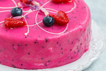 Homemade mousse cake with pitahaya and fresh berries. Decorated with blueberries, raspberries, flower petals and white chocolate on a light background close-up.  selective focus