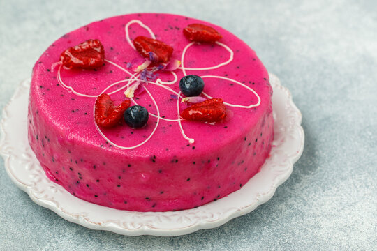 Homemade mousse cake with pitahaya and fresh berries. Decorated with blueberries, raspberries, flower petals and white chocolate on a light background.  selective focus