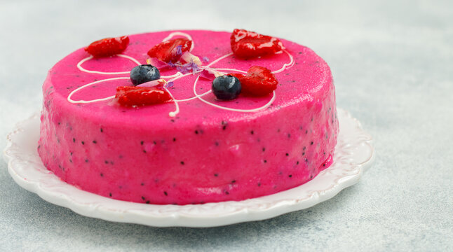 Homemade mousse cake with pitahaya and fresh berries. Decorated with blueberries, raspberries, flower petals and white chocolate on a light background.  selective focus