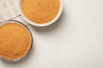 Brown sugar in bowls on white table, flat lay. Space for text