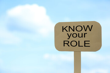 Cardboard sign with phrase Know Your Role against cloudy sky, space for text