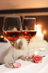 Wine in glasses and rose on edge of bath indoors, closeup. Romantic atmosphere