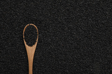 Wooden spoon on pile of black sesame seeds, top view. Space for text
