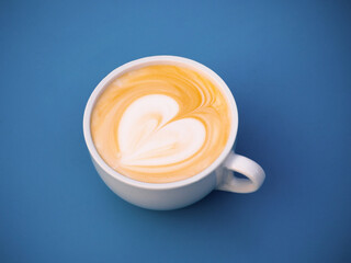 Cup of cappuccino with latte art in the form of a heart on a blue surface