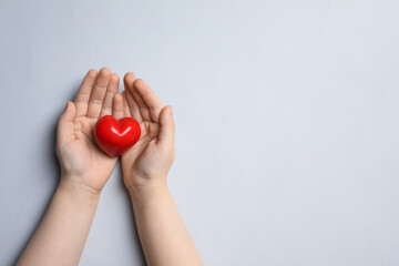 Child holding red heart on light grey background, top view. Space for text