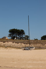 A boat lying on the sand of the beach. a quatamaran is placed on the beach, the sky is blue, trees...