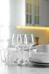 Different clean dishware and glasses on white marble table in kitchen