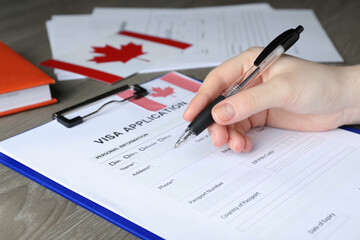 Woman filling visa application form to Canada at table, closeup