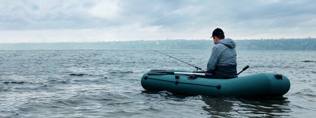 Man fishing with rod from inflatable rubber boat on river, space for text. Banner design