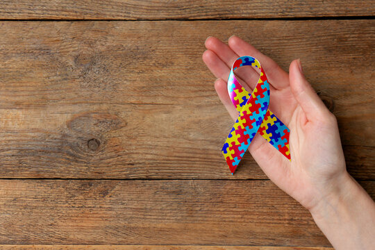 World Autism Awareness Day. Woman with colorful puzzle ribbon on wooden background, top view with space for text