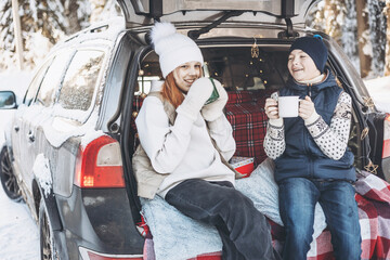 Two friends teenagers boy and girl with thermos sitting in trunk of car decorated for Christmas....