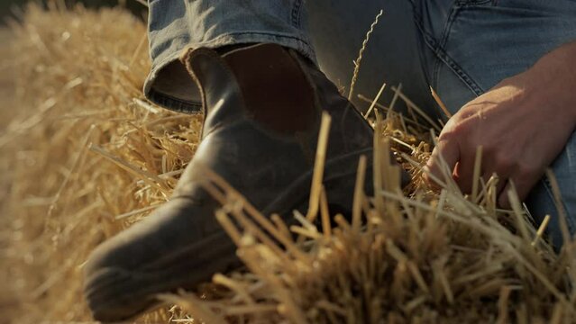 Closeup farmer dusty boot on hay stack closeup. Field worker resting on dry bale
