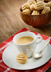 Cup of coffee with a bowl of mini churro, on a wooden table with red checkers fabric