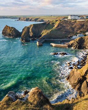 View of historic fishing village from on cliffs to  Mullion Cove Harbour with turquiose sea at sunset, Mullion Cove, Lands End, Cornwall, United Kingdom.