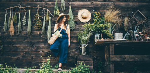 Attractive girl wearing straw hat and blue denim dungarees relaxing near wooden old summerhouse...