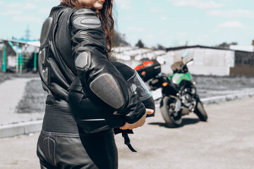 A girl in a protective motorcycle leather suit stands with her back to the background of the...