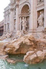 Impressive side view of one of the most famous landmarks in the world - Trevi Fountain in Rome in bright sunlight with ancient buildings in background.