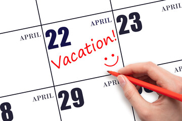 A hand writing a VACATION text and drawing a smiling face on a calendar date 22 April. Vacation...