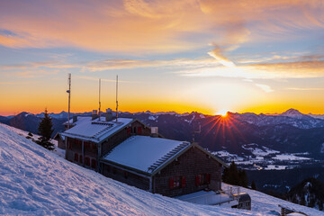 Colorful winter sunrise with sun rays above ridge and mountain hut