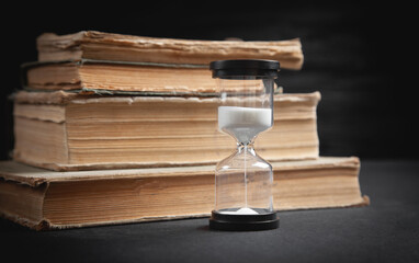 Book and hourglass on the black table.