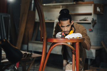 Young Asian man Carpenter uses a tape measure to measure chair on the workbench in woodcraft carpentry workshop.