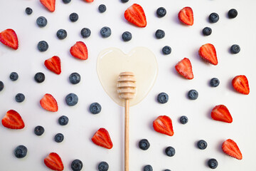 Natural honey in the form of a heart with a wooden stick and with blueberries and strawberries 