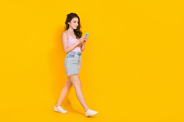 Fototapeta na wymiar Full length photo of pretty sweet lady dressed pink singlet walking typing modern device isolated yellow color background