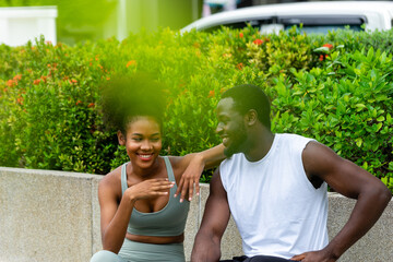 A black American man and woman couples resting after exercising in the garden chatting and smiling cheerfully at each other.