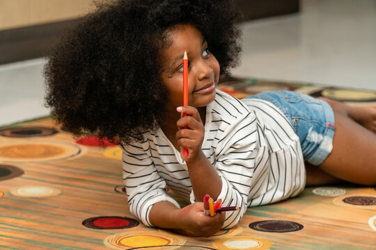 A black American girl smiles at her mother with colored pencils in her living room.