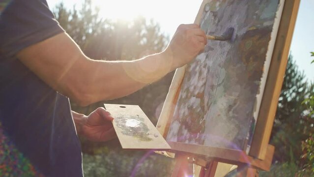 The artist painter a picture in nature. Hobbies outdoors in sunny weather. Painting on canvas on an easel