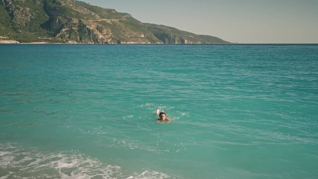 4k slow motion footage of man swims to shore in turquoise water of mediterranean sea in Oludeniz Beach in Aegean Sea after swimming. Summer tourist Season Fethiye, Mugla Turkey
