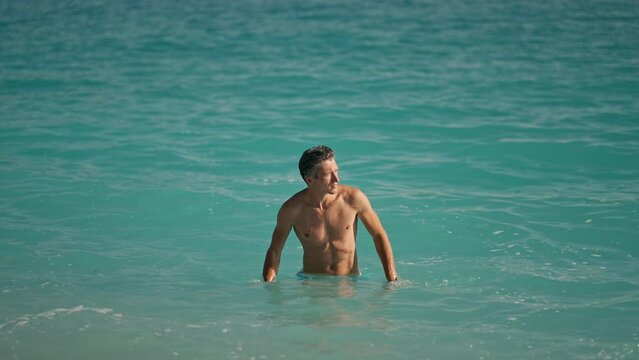 slow motion of muscular athletic man on beach in turquoise water of mediterranean sea in Oludeniz Beach in Aegean Sea after swimming. Summer tourist Season Fethiye, Mugla Turkey