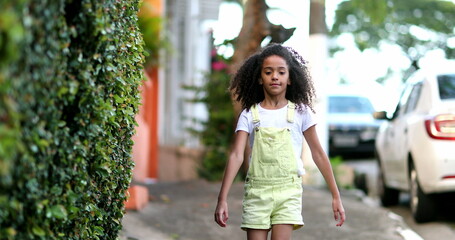 Mixed race little girl walking otuside on city sidewalk