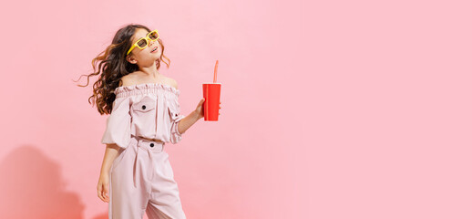 Fashionable little girl, kid posing isolated over pink color background. Concept of children emotions, fashion, happy childhood, beauty, school and ad