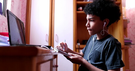 Mixed race kids doing homework at home writing on notepad and looking at laptop screen