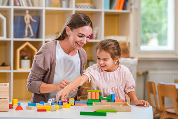 Kindergarten teacher playing together with children in the colorful preschool classroom. Mother...