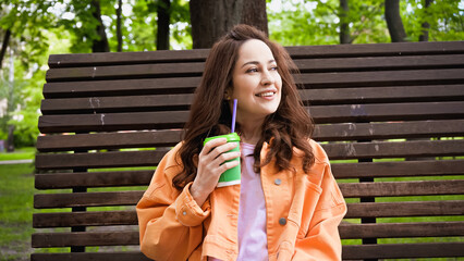 happy woman holding coffee to go with straw in park.