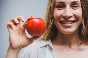 Cute brunette woman in white shirt holding red apple in hand standing on isolated white background dietetics and nutrition. Healthy food