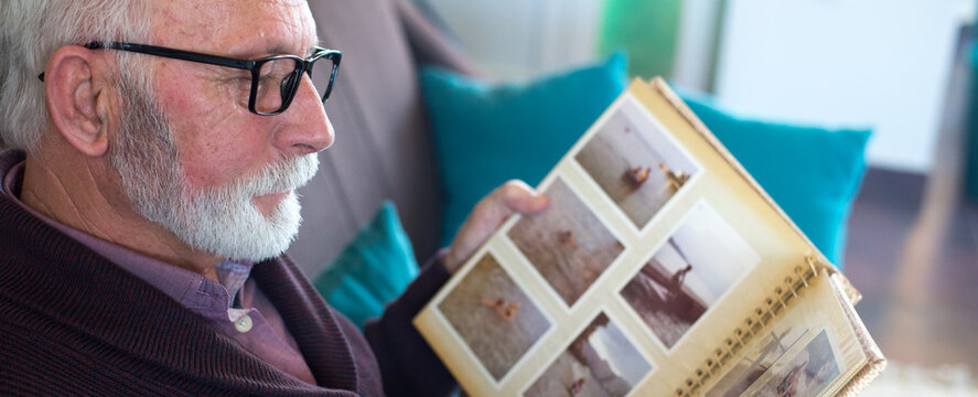 Senior man looking at photos in photo album with photographs from his childhood