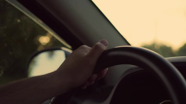 Close up of man's hand on steering wheel of car on background of sunset outside window cabin. Concept of traveling and free lifestyle