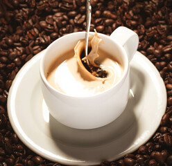Löffel fällt in eine Kaffeetasse umringt von Kaffeebohnen und verschüttet Kaffee