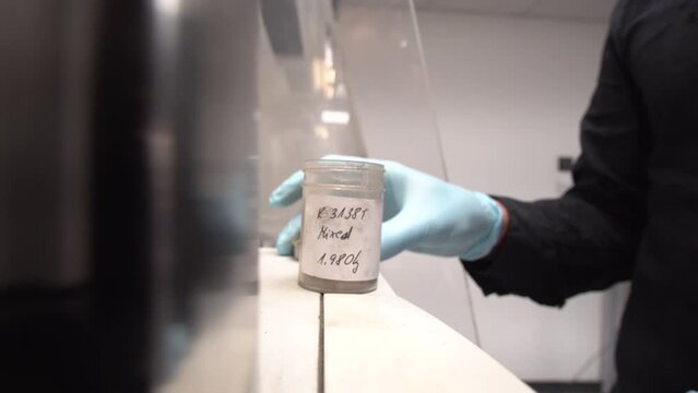 Research lab worker opens sample container lid with grey dry powder in
